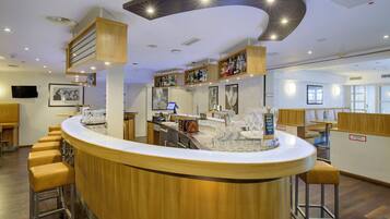 Zona de bar con barra curva, taburetes y una variedad de botellas y vasos.