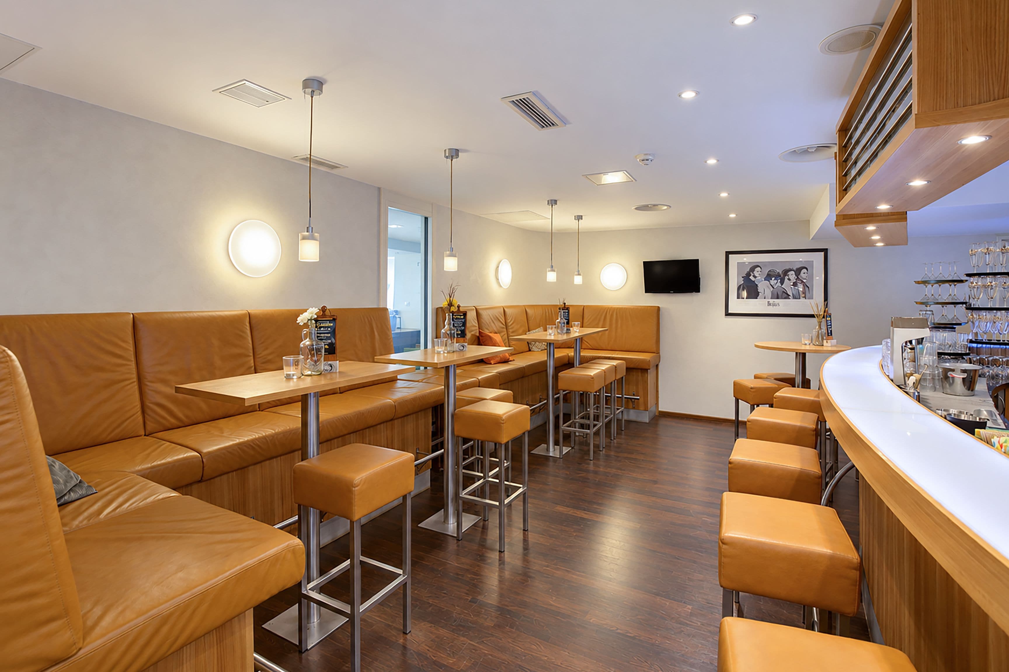 A modern restaurant interior with leather booths, bar stools, and pendant lighting.