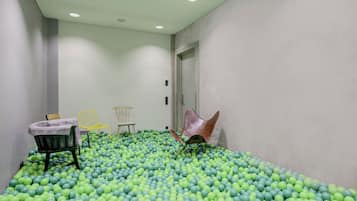 Una habitación con un piso cubierto de bolas verdes y azules, una puerta y tres sillas.