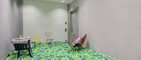 A room with a floor covered in green and blue balls, a door, and three chairs.