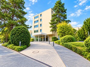 A modern building with a paved entrance, surrounded by well-maintained greenery and trees. - Seminaris Sunday Hotel Bad Honnef (Bad Honnef)