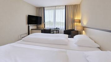 Ein Hotelzimmer mit einem Bett, einem Schreibtisch, einem Stuhl, einem Fernseher und einem Fenster mit Vorhängen.