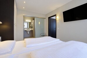 A hotel room with a bed, a bedside table, a flat-screen TV mounted on the wall, and a bathroom visible through an open door. - Seminaris Sunday Hotel Bad Honnef (Bad Honnef)