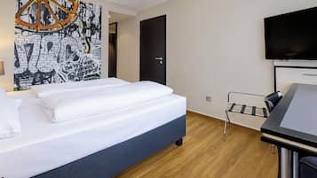 Une chambre d’hôtel équipée d’un lit, d’un bureau, d’une chaise, d’une télévision et d’un mur orné d’un motif graphique.