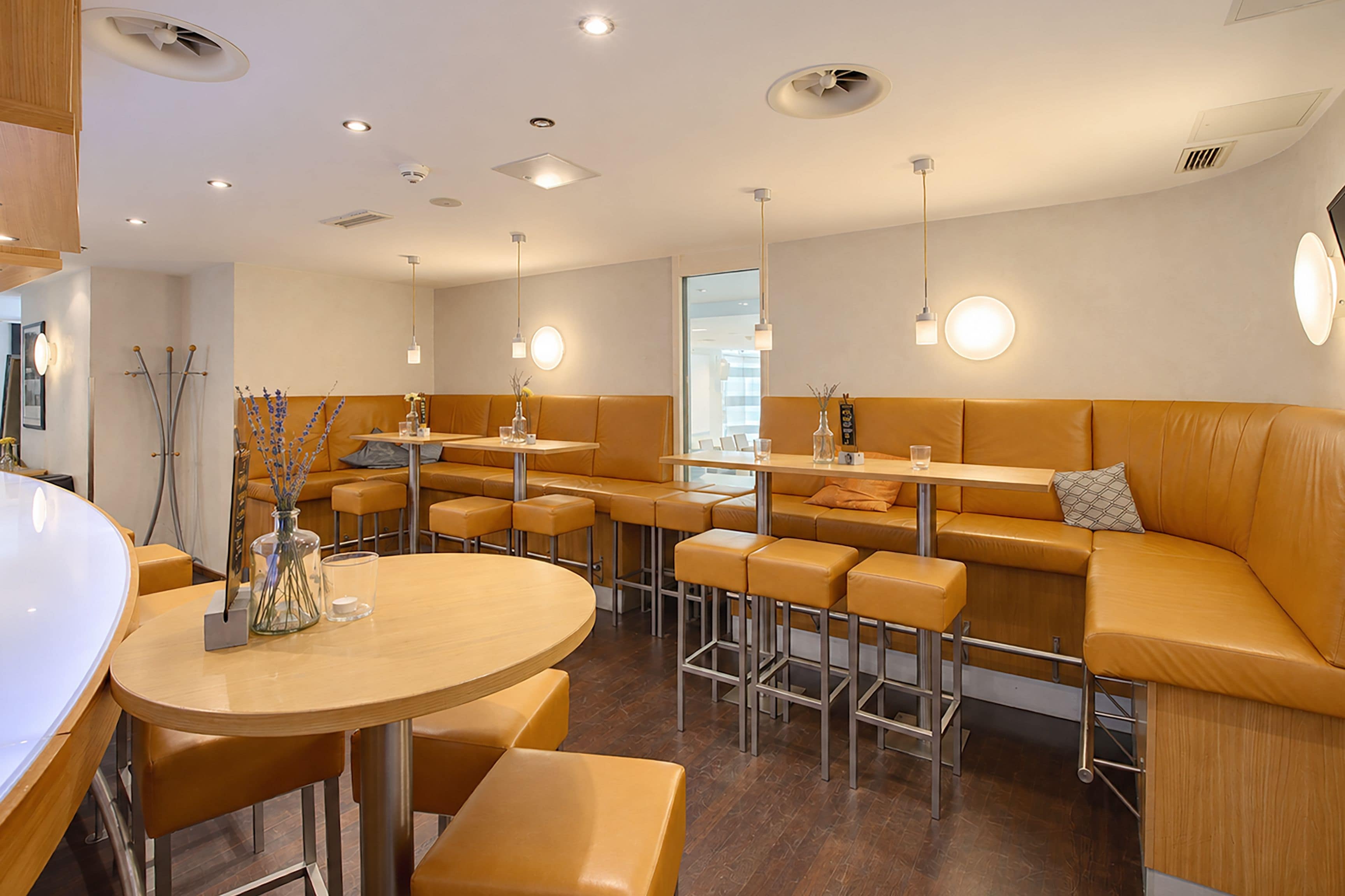 A modern restaurant interior with round tables, high stools, and cushioned seating.
