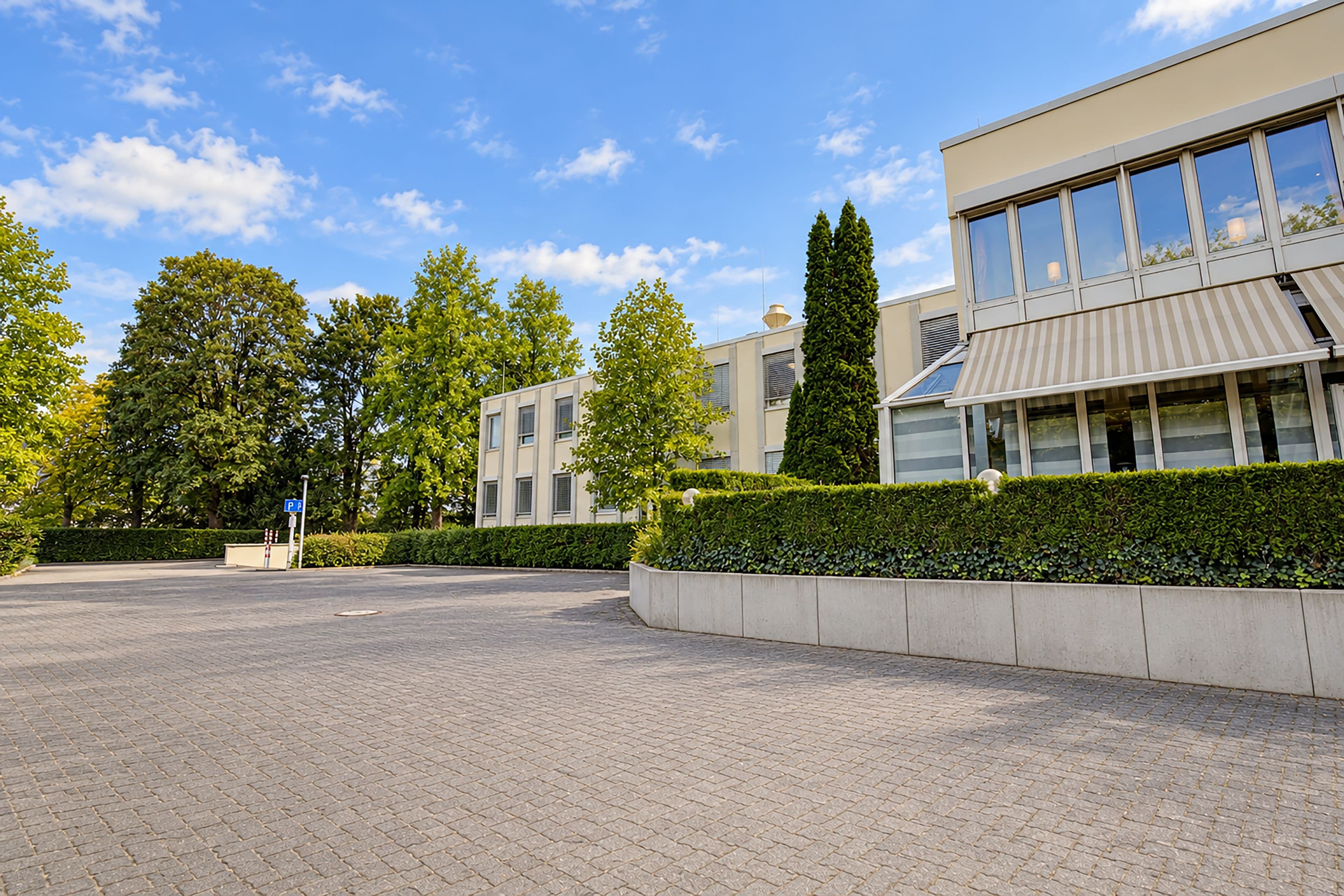 A paved parking area with a building featuring large windows and a striped awning.
