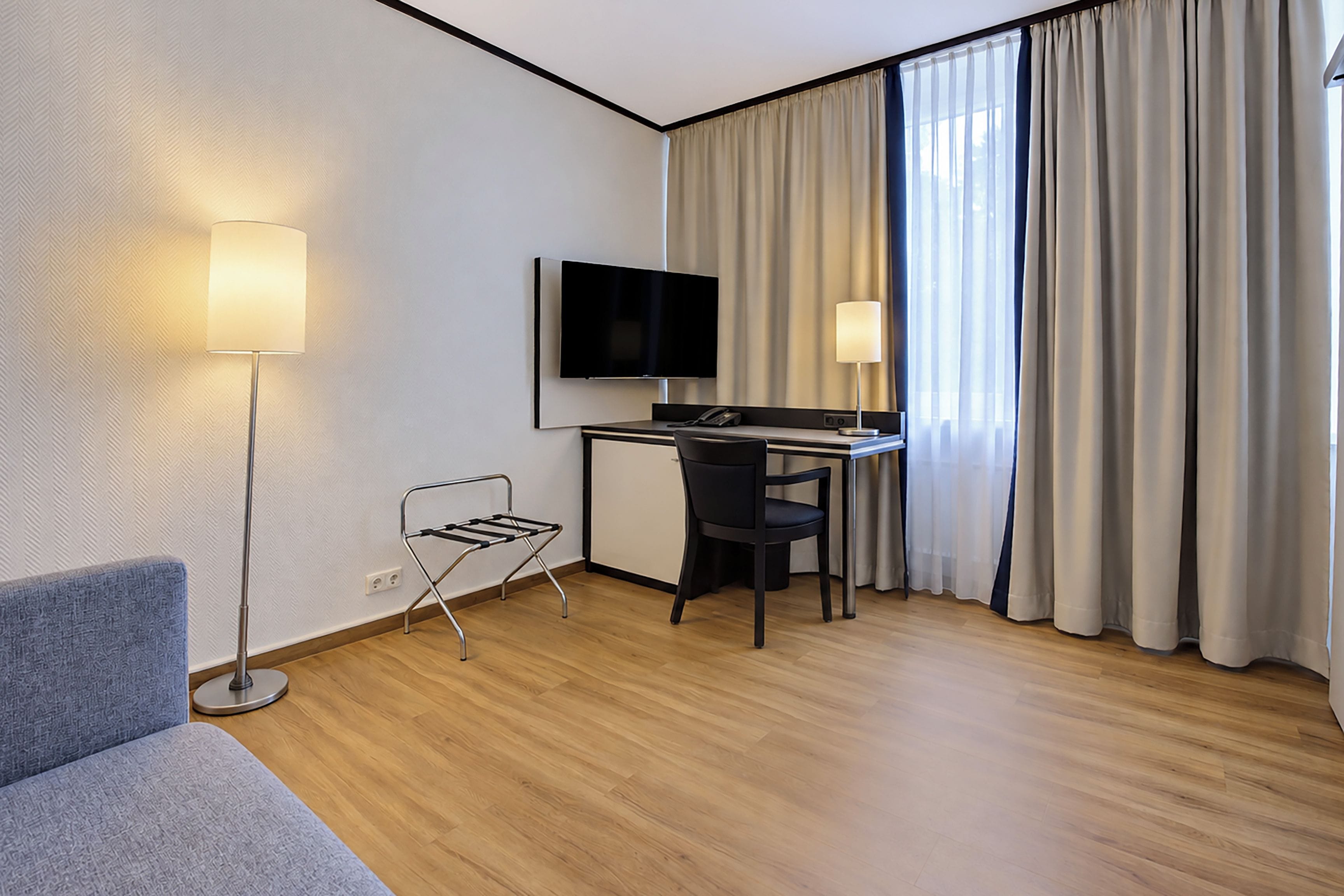 Une chambre d’hôtel équipée d’un bureau, d’une chaise, d’une télévision et d’une lampe sur pied.