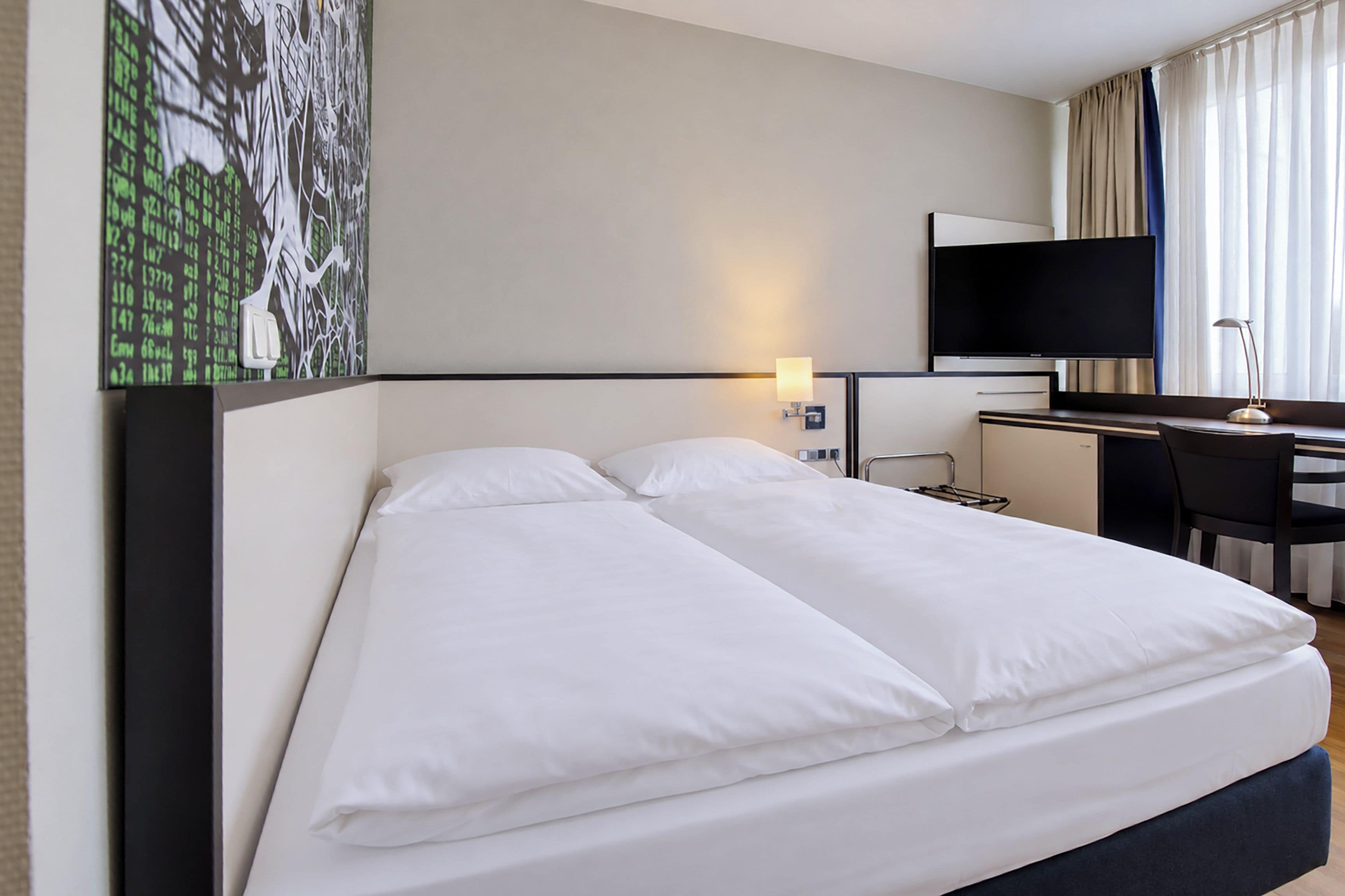 A hotel room with a bed, a desk, a chair, a television, and a painting on the wall.