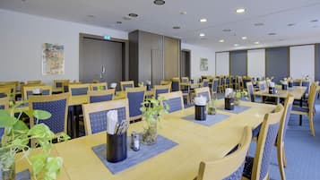 Een vergaderzaal met meerdere tafels en stoelen, voorzien van naambordjes, pennen en schriften.