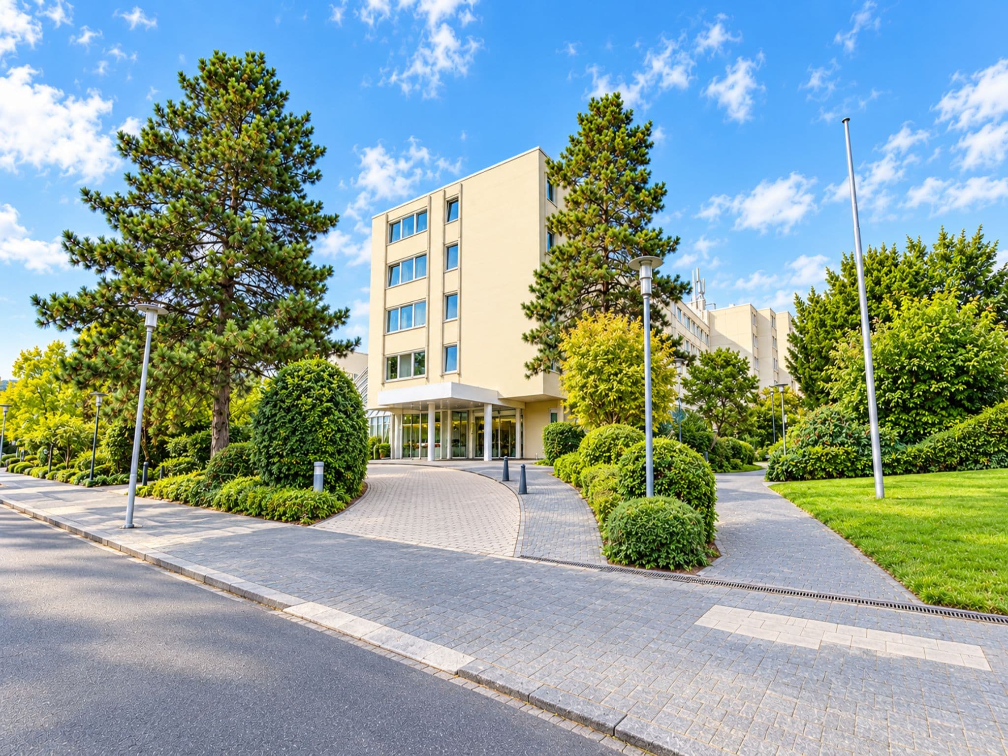 A modern building with a paved entrance, surrounded by well-maintained greenery and trees.
