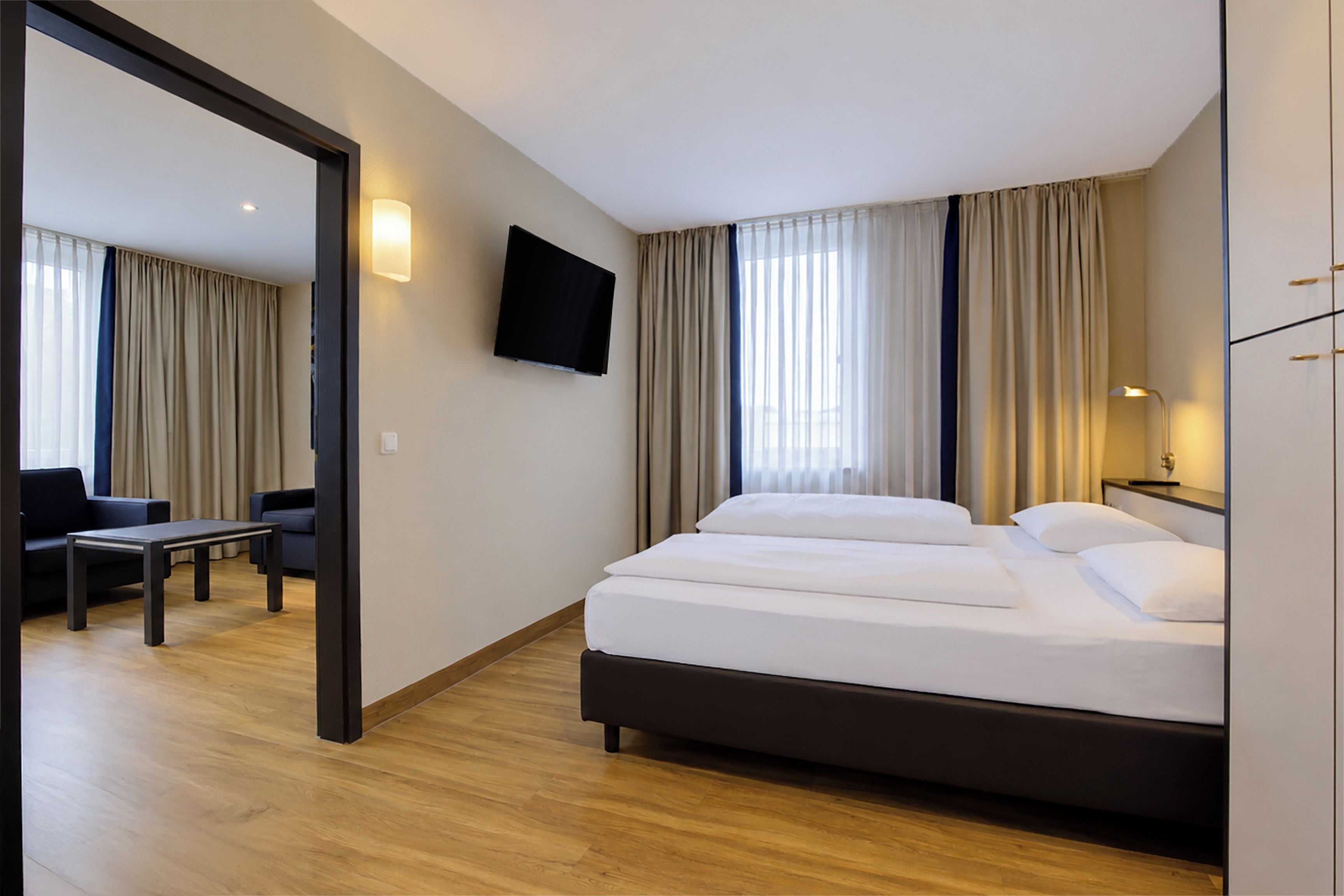 A hotel room with a bed, a TV mounted on the wall, a desk, and a chair.