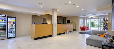 Una moderna zona de recepción con mostrador, refrigerador de Pepsi y un área de estar con sofá y mesa de centro.
