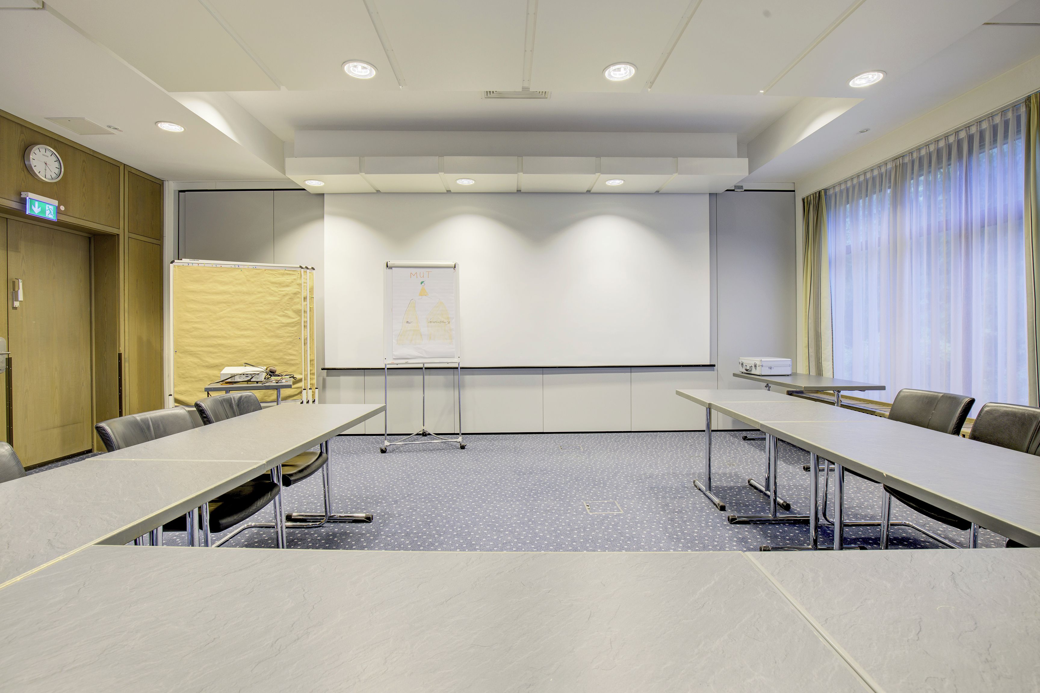Een vergaderruimte met een projectiescherm, een whiteboard en een groot raam met gordijnen.