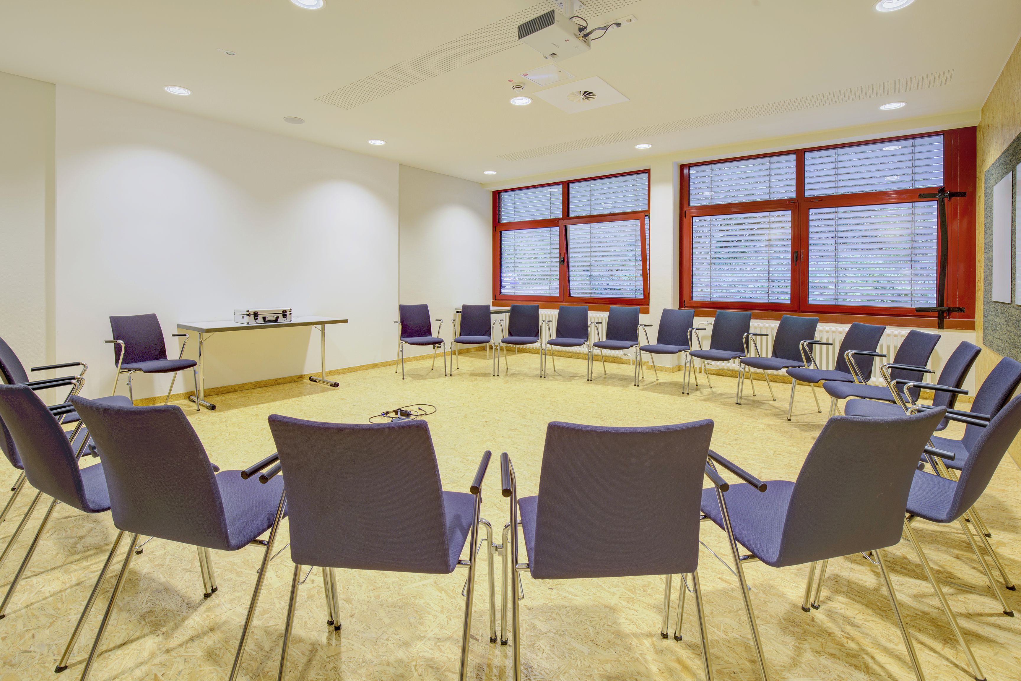 A conference room with a circular table, multiple chairs, and large windows with blinds.
