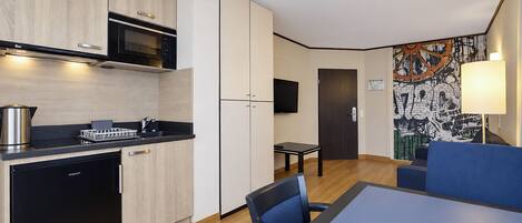 Cocina compacta con microondas, lavaplatos y fregadero. Zona de comedor con mesa y sillas.