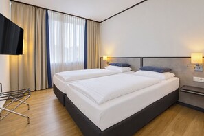 A hotel room with two beds, a TV, a lamp, and a window with curtains. - Seminaris Sunday Hotel Bad Honnef (Bad Honnef)