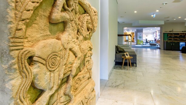 Un relieve de piedra con diseños intrincados, un interior moderno con piso de mármol y un rincón de estar con una pequeña mesa y sillas.