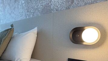 A hotel room with a bed, a wall-mounted light, a control panel, and a textured wall.