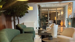A modern lounge area with green and white sofas, a round coffee table, and a potted plant. - The Originals City, Le Patio, Cholet Nord (Beaupreau-en-Mauges)