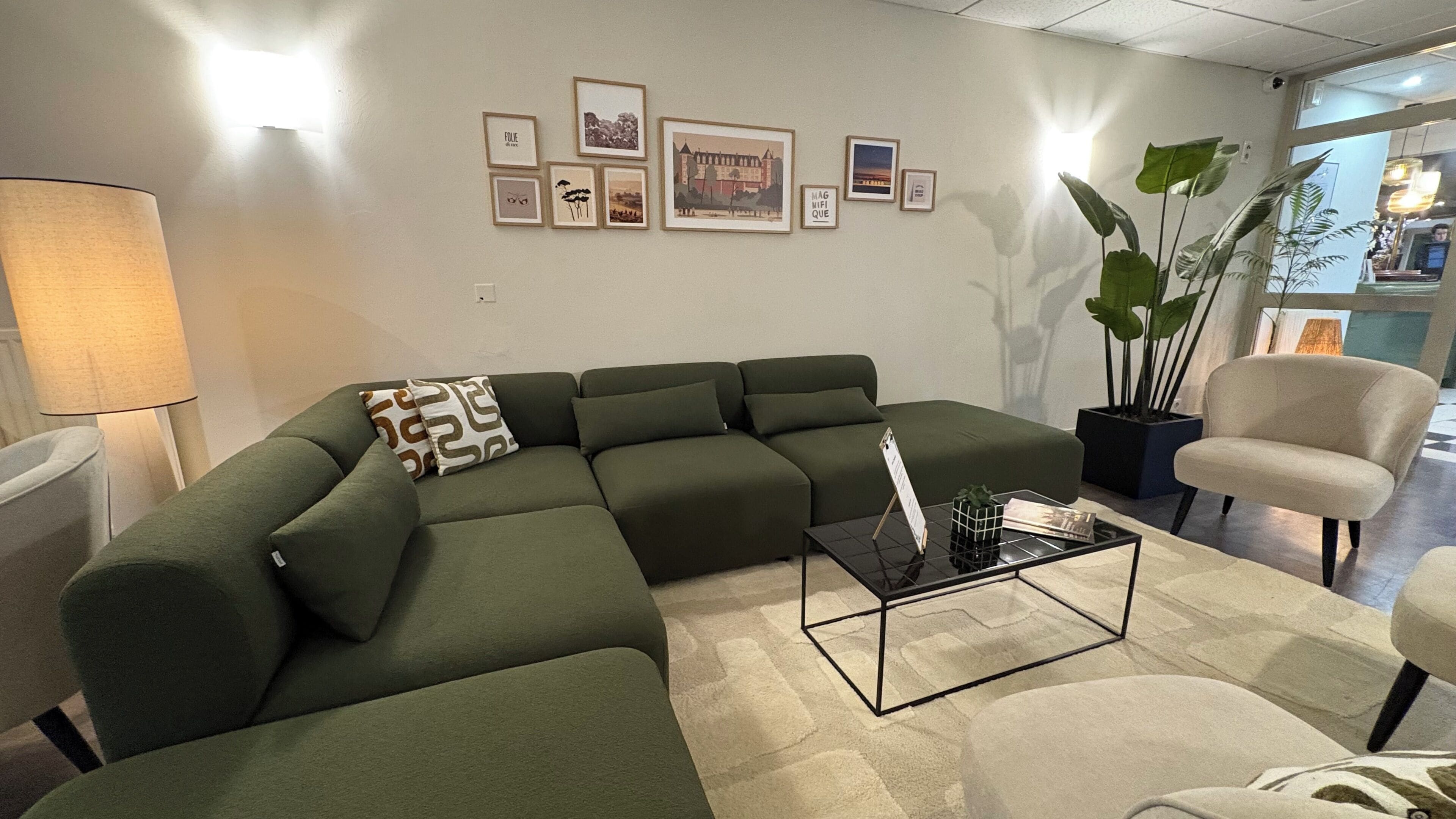 Una sala de estar con sofá seccional, una mesa de centro, una lámpara y cuadros en la pared.