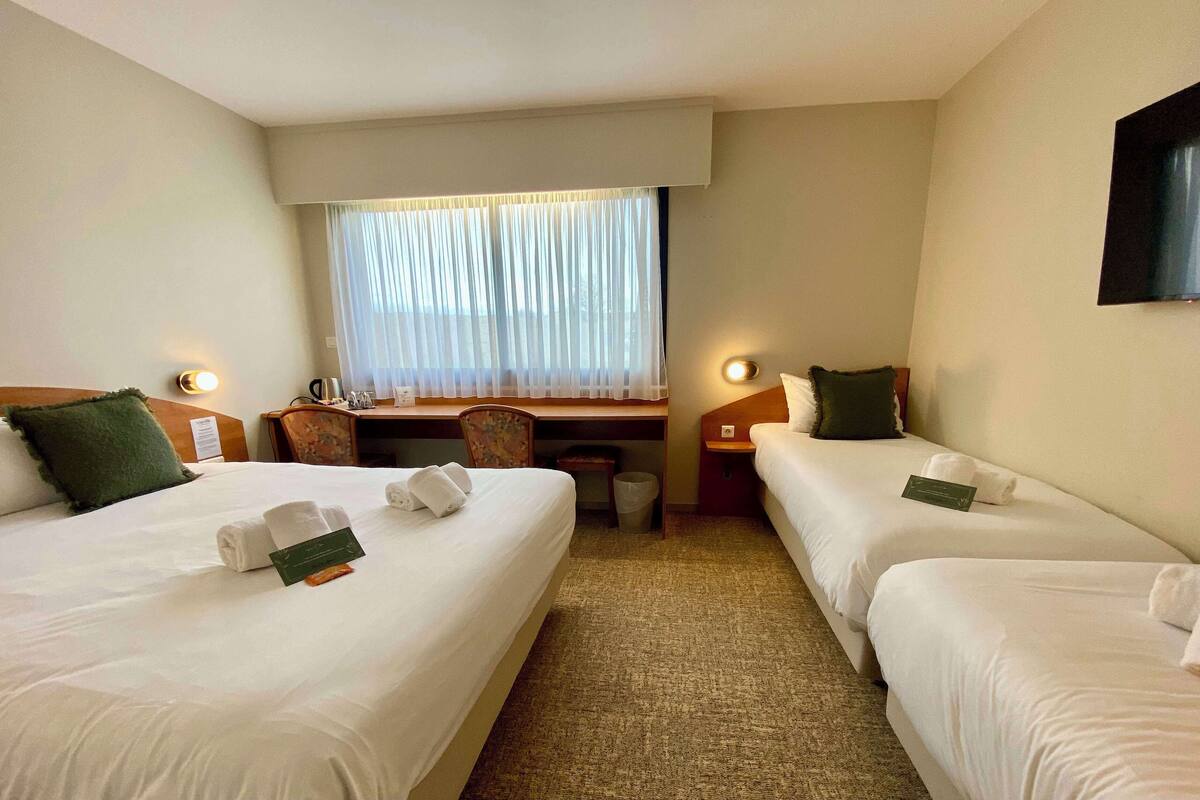 A hotel room with two beds, a desk, a chair, and a TV on the wall.