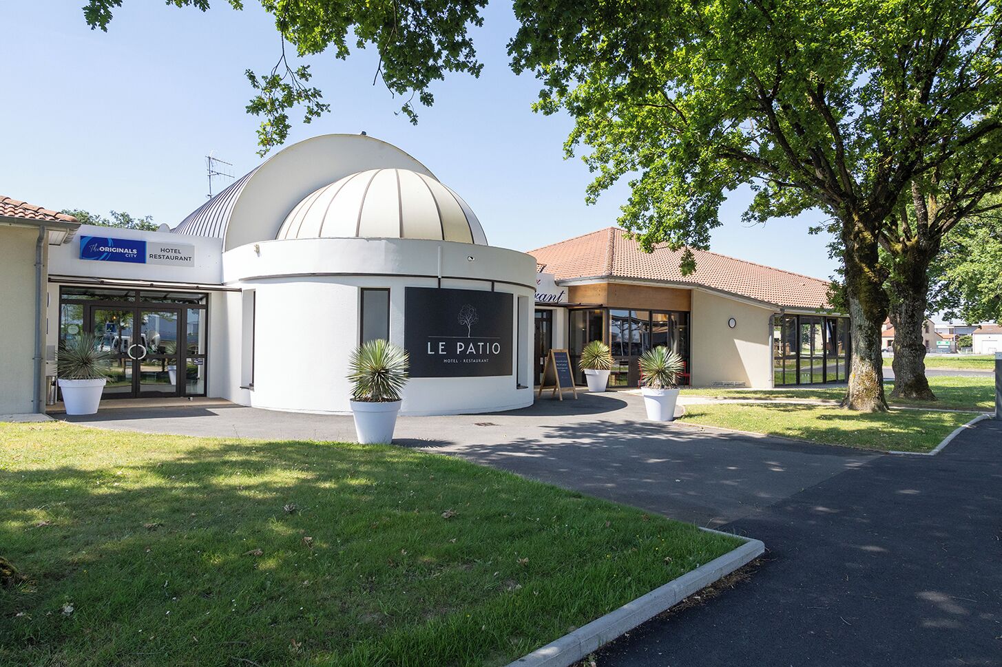 A hotel with a dome-shaped building, a sign reading 'LE PATIO HOTEL RESTAURANT,' and potted plants in front.