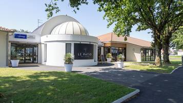 A hotel with a dome-shaped building, a sign reading 'LE PATIO HOTEL RESTAURANT,' and potted plants in front.