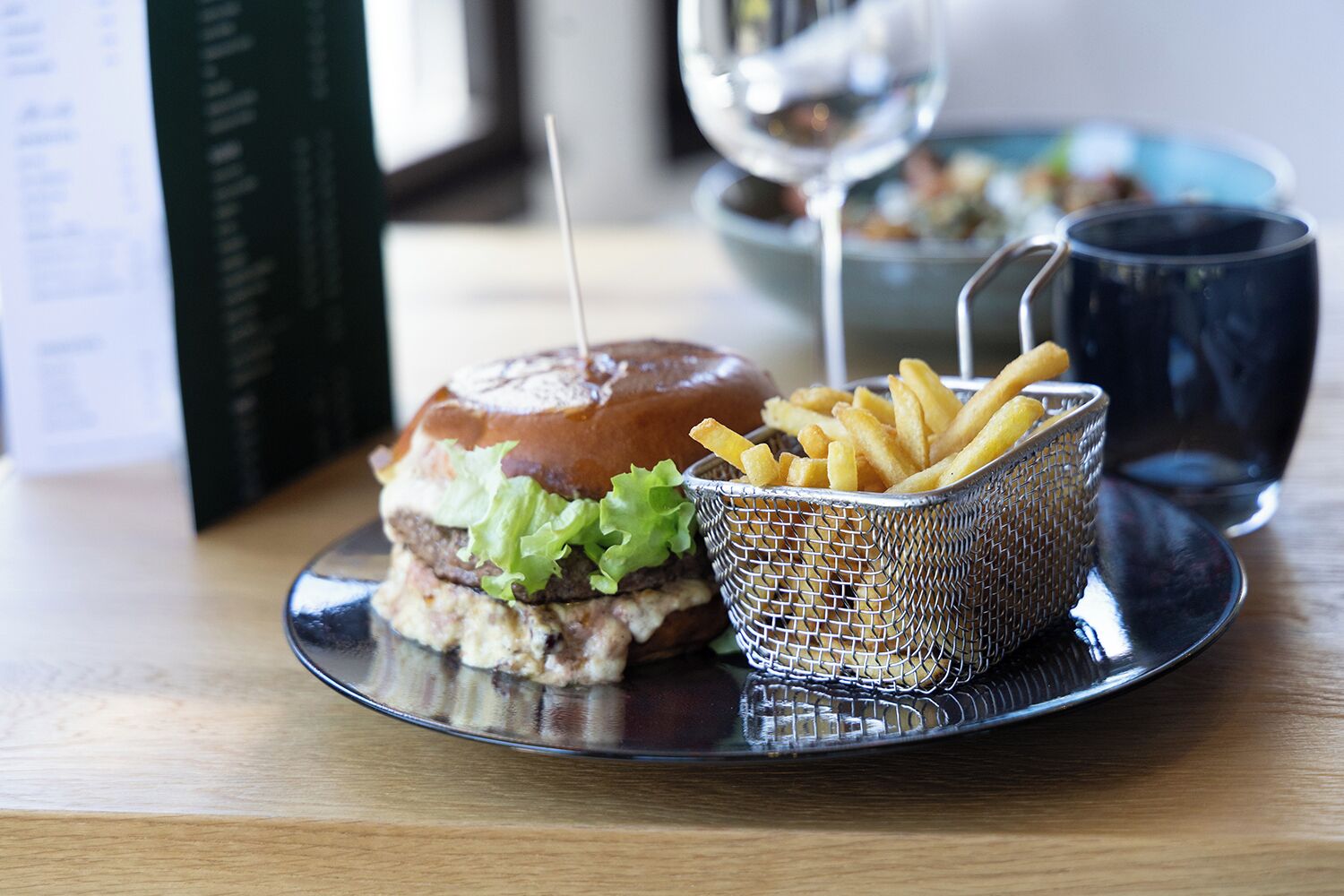 Una hamburguesa con papas fritas en un plato, un vaso de agua y un menú sobre la mesa.