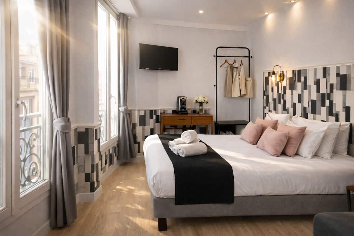A modern hotel room with a large bed, a desk, a TV, and a view of the city.