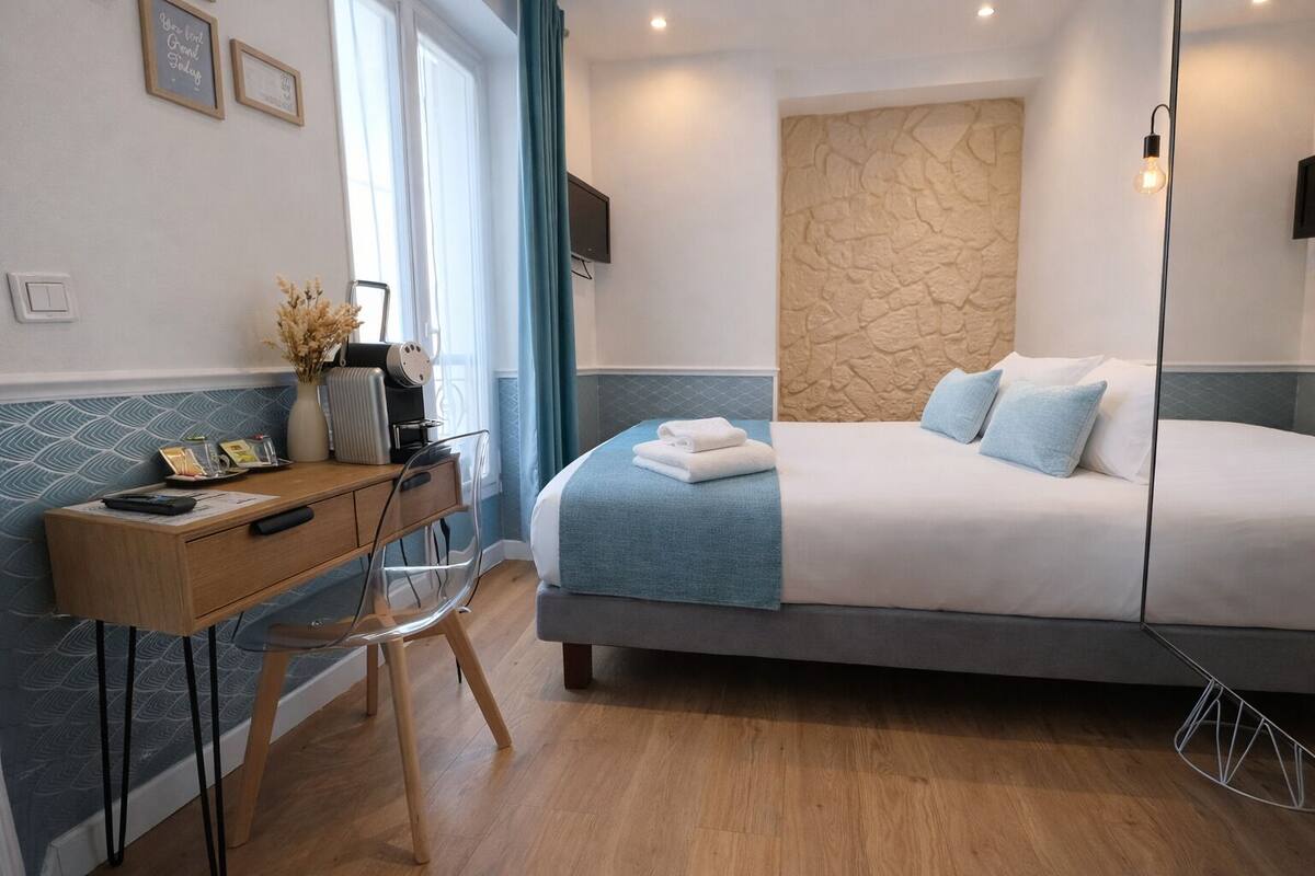 A modern hotel room with a bed, desk, chair, and a stone-textured wall.