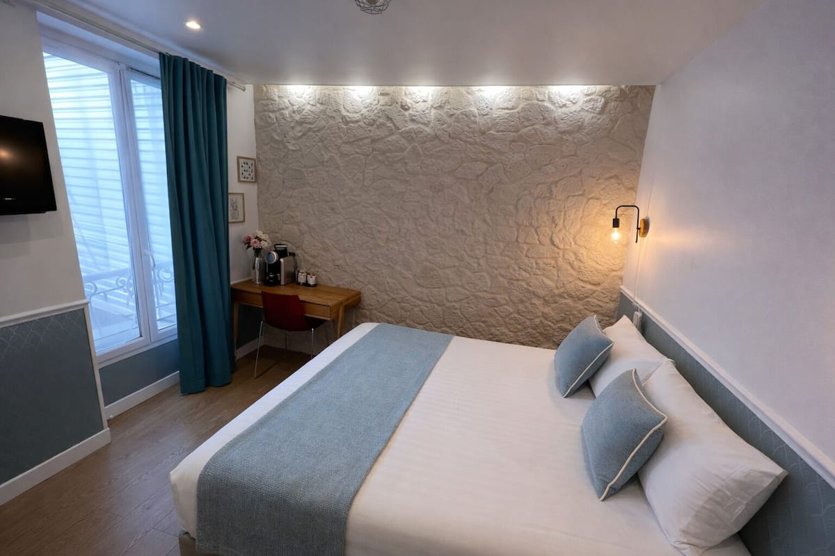 A bedroom with a bed, a desk, a chair, a TV, and a stone-textured wall.