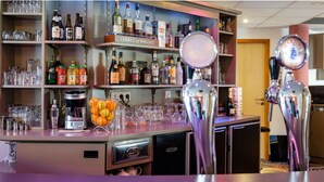 Un espace bar avec des étagères remplies de différentes bouteilles et de verres, un panier de fruits et une machine à café.