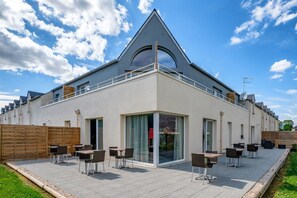 A modern building with a triangular roof and large windows. It has outdoor seating with tables and chairs.