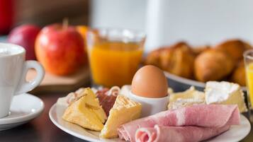 A breakfast plate with cheese, ham, an egg, and croissants.