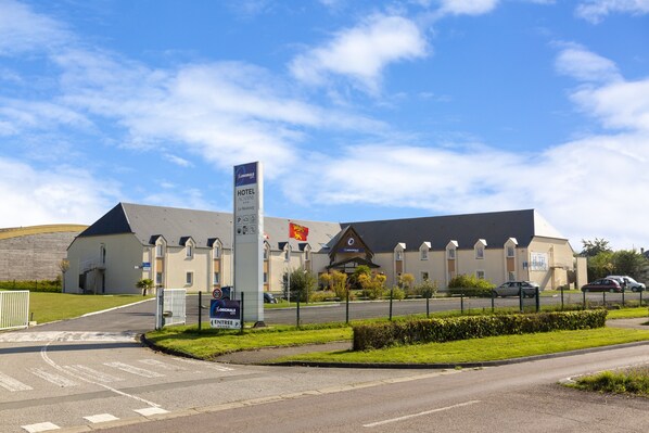 A hotel with a prominent entrance, a parking area, and a well-maintained lawn.