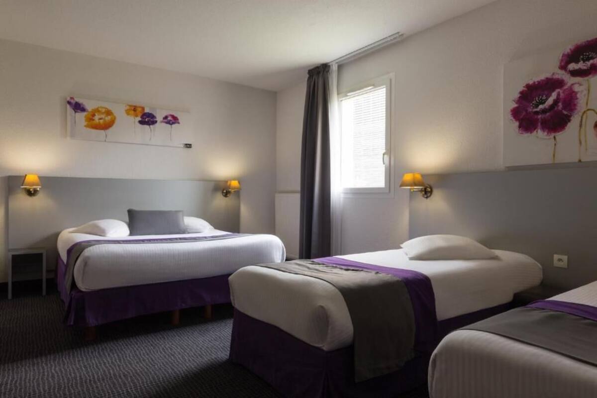 Una habitación de hotel con dos camas, un escritorio pequeño y una ventana con cortinas.