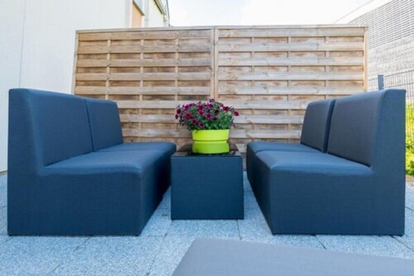 A modern outdoor seating area with two dark blue sofas and a small table, set against a wooden fence backdrop.