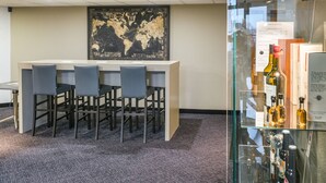 Un espace bar avec un long comptoir et quatre chaises, une carte du monde accrochée au mur et une vitrine en verre contenant des bouteilles.