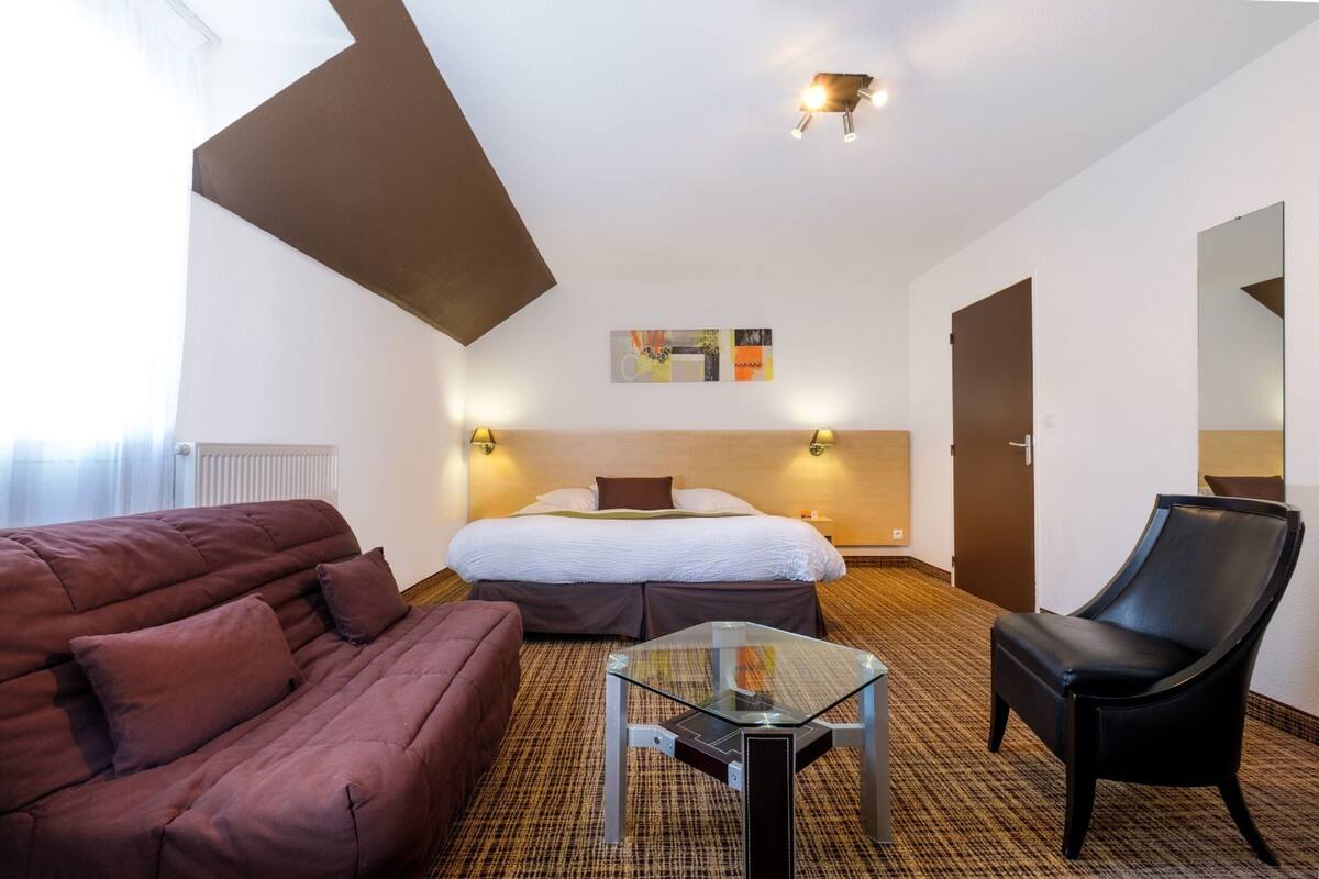 Habitación de hotel con cama, una mesa de centro de vidrio, un sofá, una silla y una obra de arte colgada en la pared.