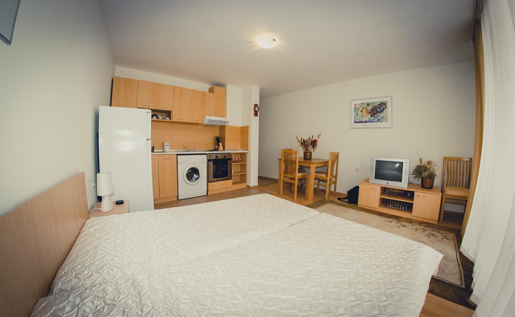 A hotel room with a bed, a kitchenette, a dining area, and a TV.