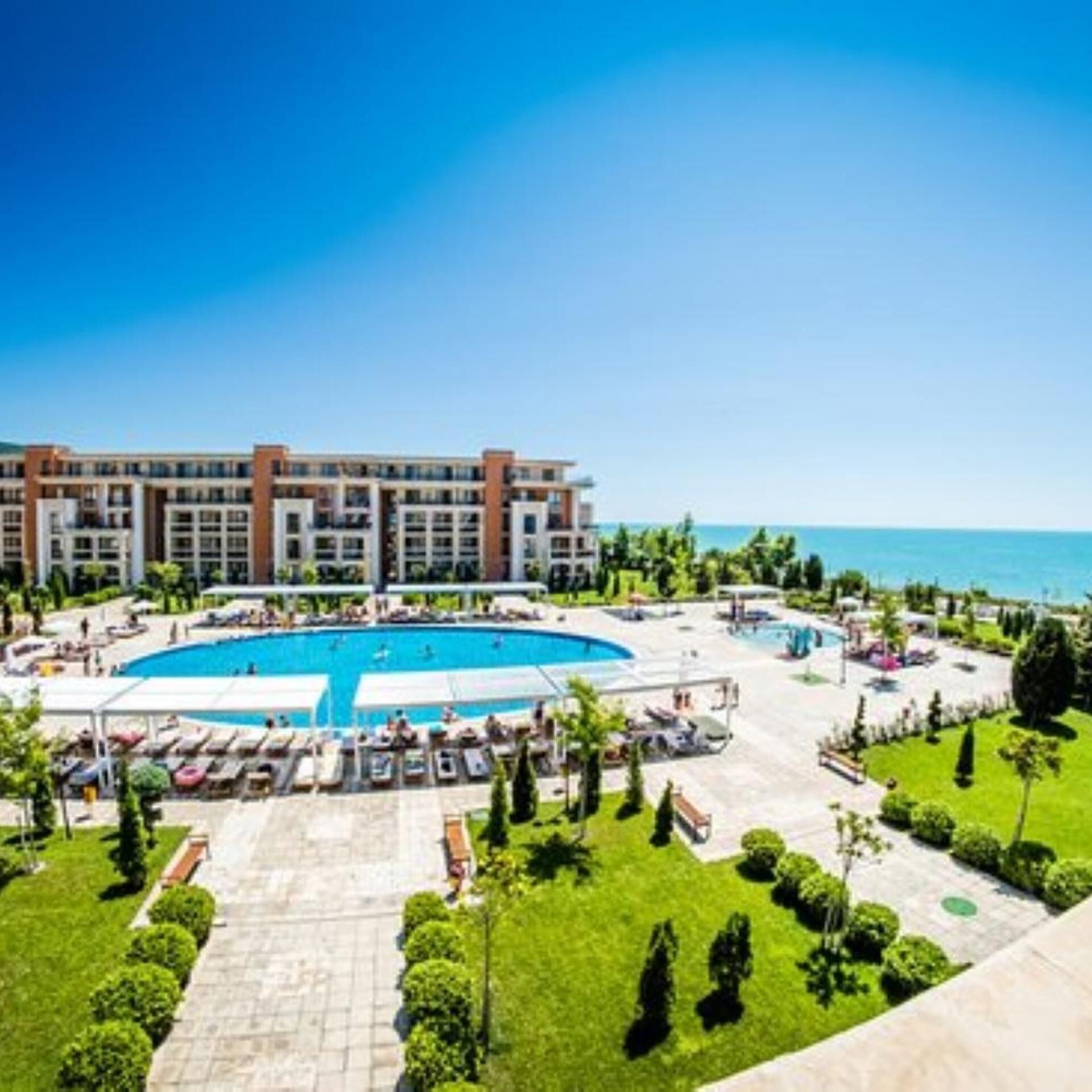 A hotel with a central pool surrounded by lounge chairs and a landscaped garden.