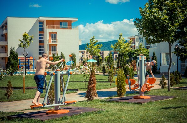 A hotel with outdoor exercise equipment, a pool, and a playground.