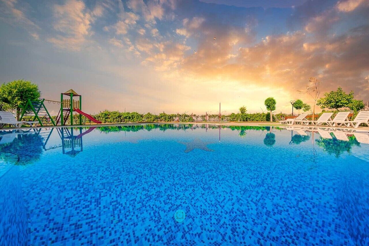 A swimming pool with a slide and a climbing structure, surrounded by lounge chairs and trees.