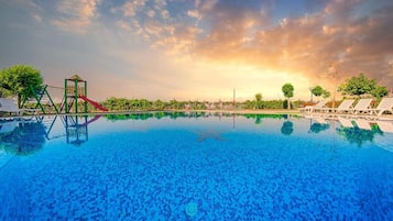 A swimming pool with a slide and a climbing structure, surrounded by lounge chairs and trees.