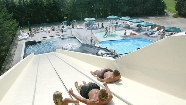 Tobogán de agua en un complejo turístico con piscina, sillones de descanso y sombrillas.