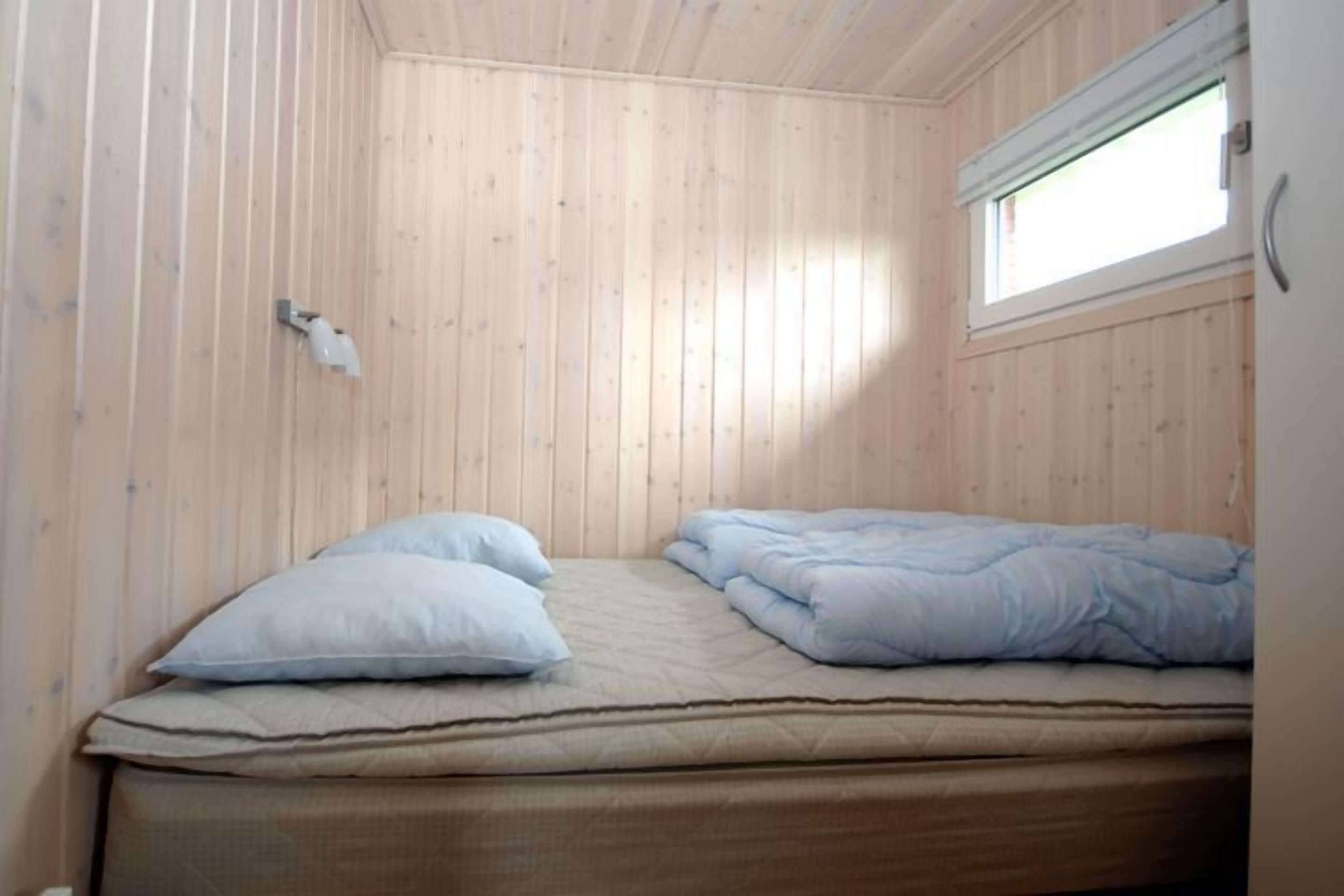 A small, single-bed room with wooden walls and a window.