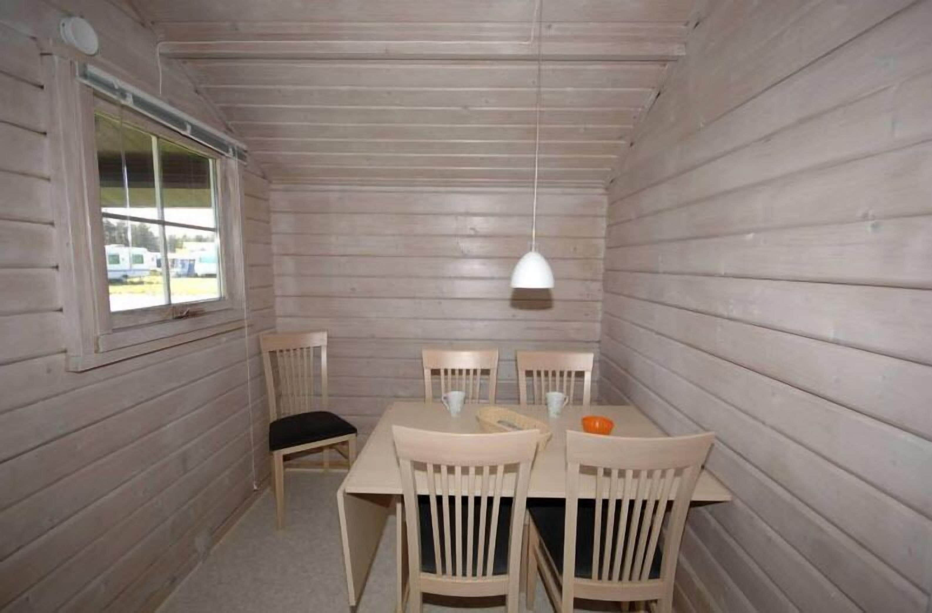 A dining area with a wooden table and chairs, a hanging pendant light, and a window with a view of the outside.