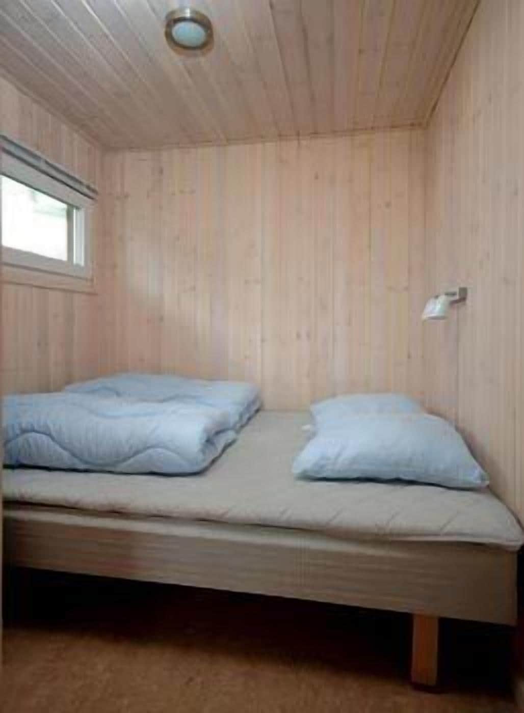 Una cama individual con colchón y almohadas en una habitación con paredes de madera y techo inclinado.