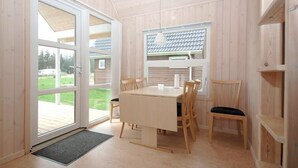 Una habitación con paneles de madera, una mesa y sillas, una ventana con vistas al exterior, y una puerta que da al exterior.