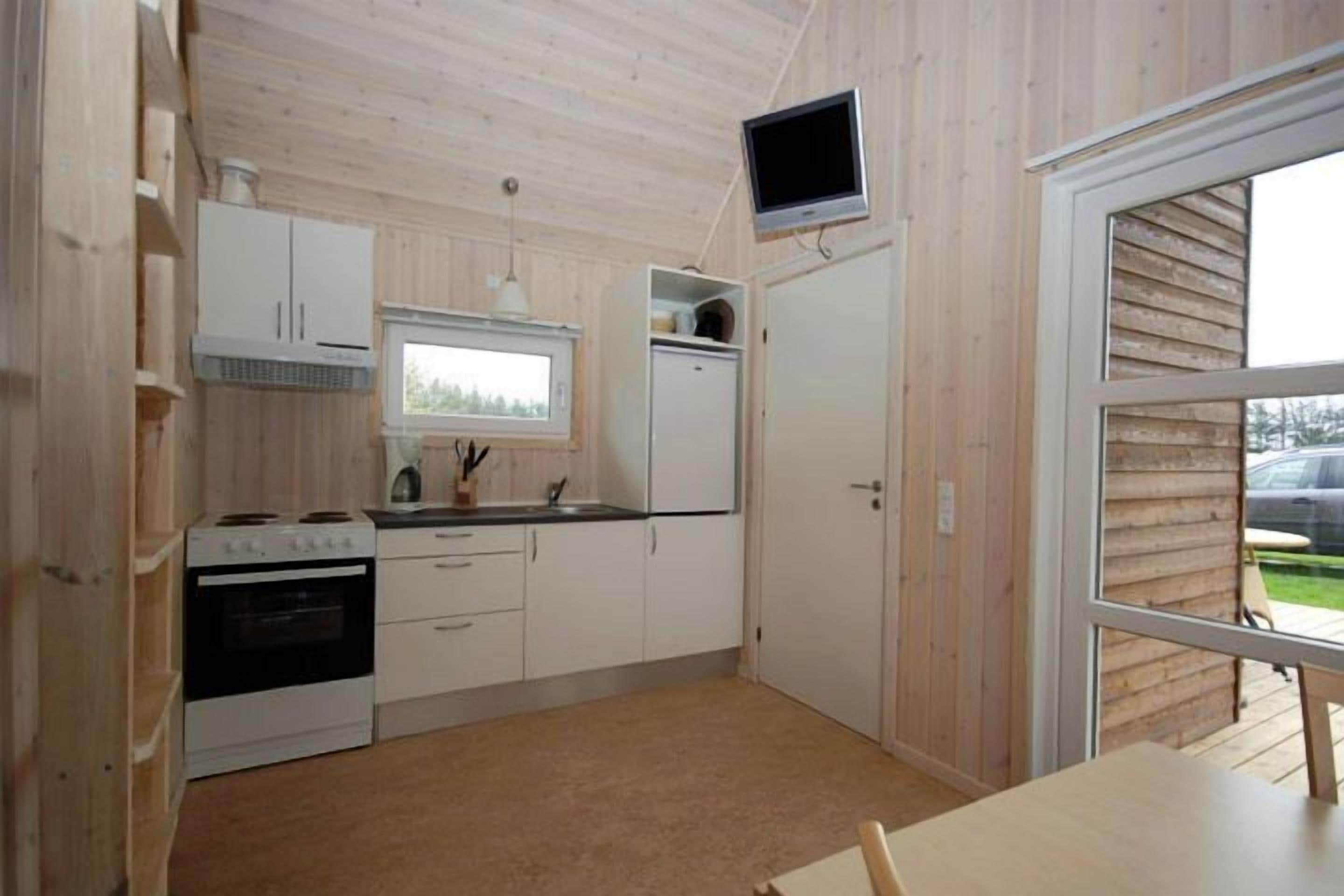 A compact kitchen with a stove, sink, and cabinets, a television mounted above the counter, and a door leading to an outdoor area.